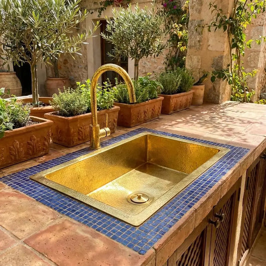Golden brass bathroom sink in Moroccan style integrated into an outdoor tiled countertop with a matching gold faucet