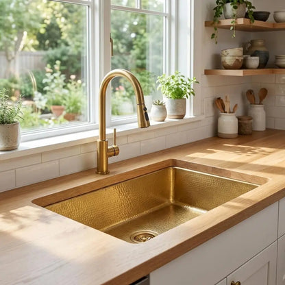 30 inch rectangular hammered copper kitchen sink installed undermount under a light wood tone countertop next to a bright window overlooking a garden