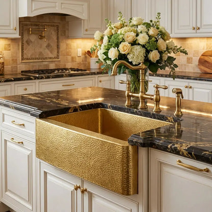 30-inch hand-hammered unlaquered brass apron front kitchen sink installed in a white kitchen island with black marble countertop
