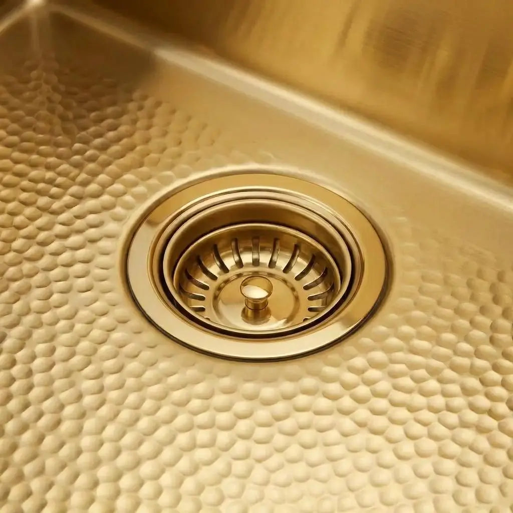 Close-up of a 30-inch unlaquered brass kitchen sink showing the standard 3.5-inch drain opening with matching basket strainer and scratch-resistant hand-hammered texture