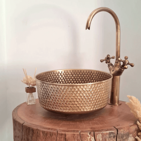 Mid-century modern hammered brass sink on wooden surface with stylish faucet and decor accessories for luxury bathroom upgrade.