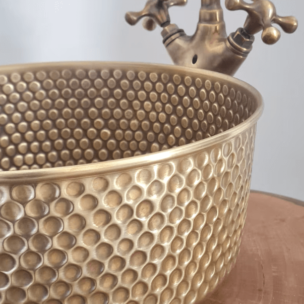 Luxury mid-century modern hammered brass sink with a textured surface and classic faucet for elegant bathroom design.