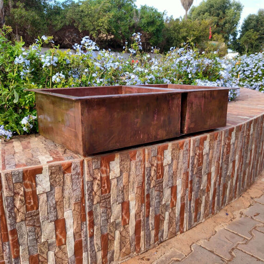 Handmade double copper sink on a brick surface surrounded by greenery and flowers, showcasing Moroccan craftsmanship.