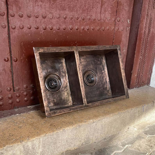 Handmade copper double vessel sink displayed on a stone surface, showcasing unique craftsmanship for kitchen or bathroom.