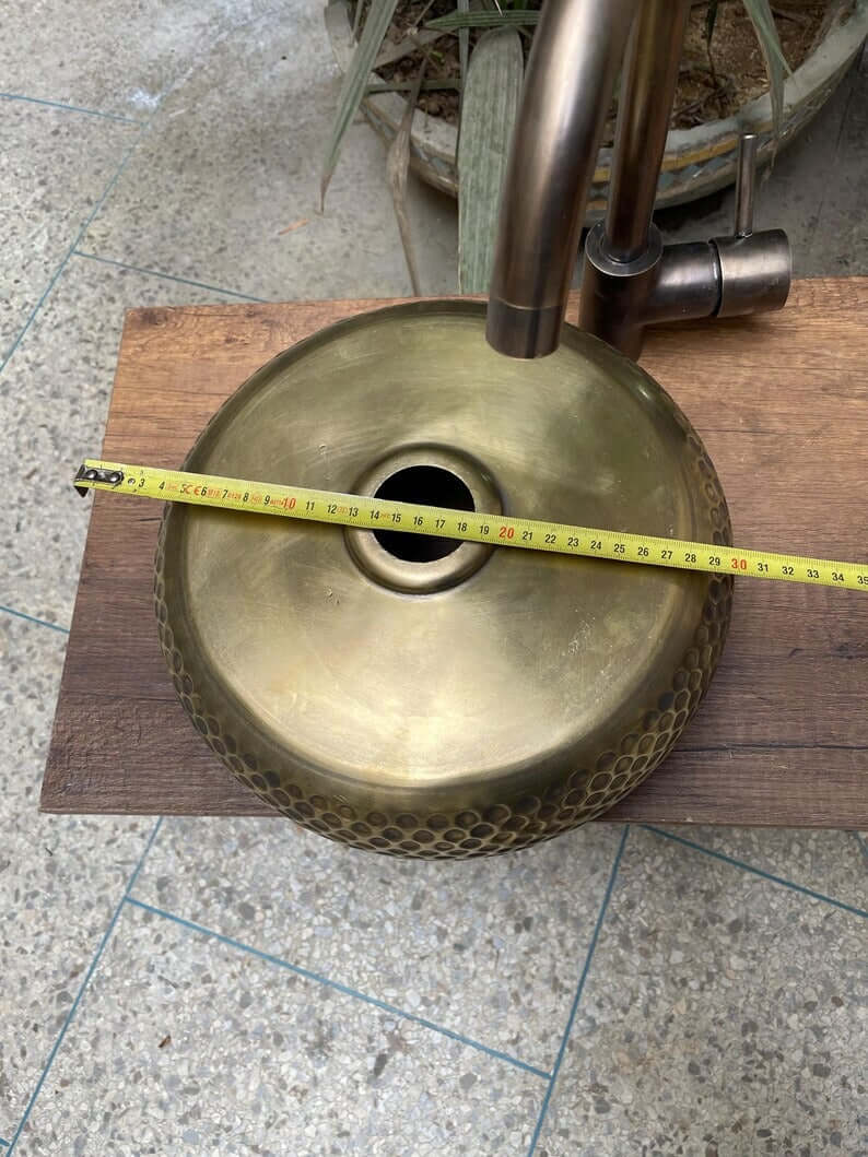Hand hammered brass kitchen sink with measuring tape, showcasing Moroccan design elegance on a wooden surface.