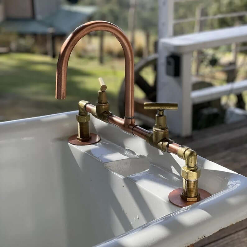 Handmade copper and brass faucet installed on a rustic sink, showcasing beautiful piping and double handles.