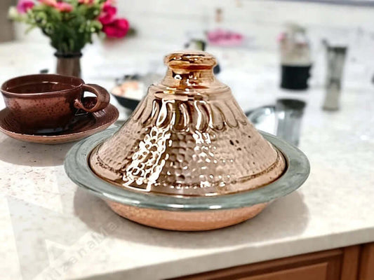 Luxurious handcrafted Moroccan copper tagine with lid and serving tray on kitchen counter, adorned with a floral pattern.