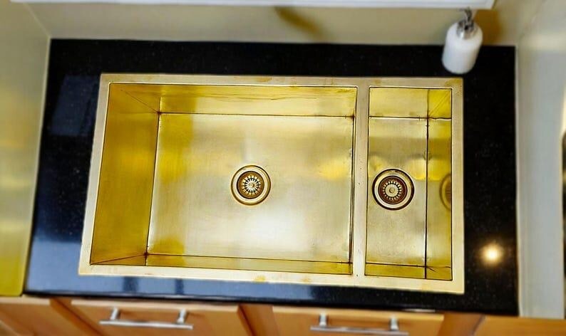 Handmade brass double square sink in a kitchen with a smooth brass finish on granite countertop.