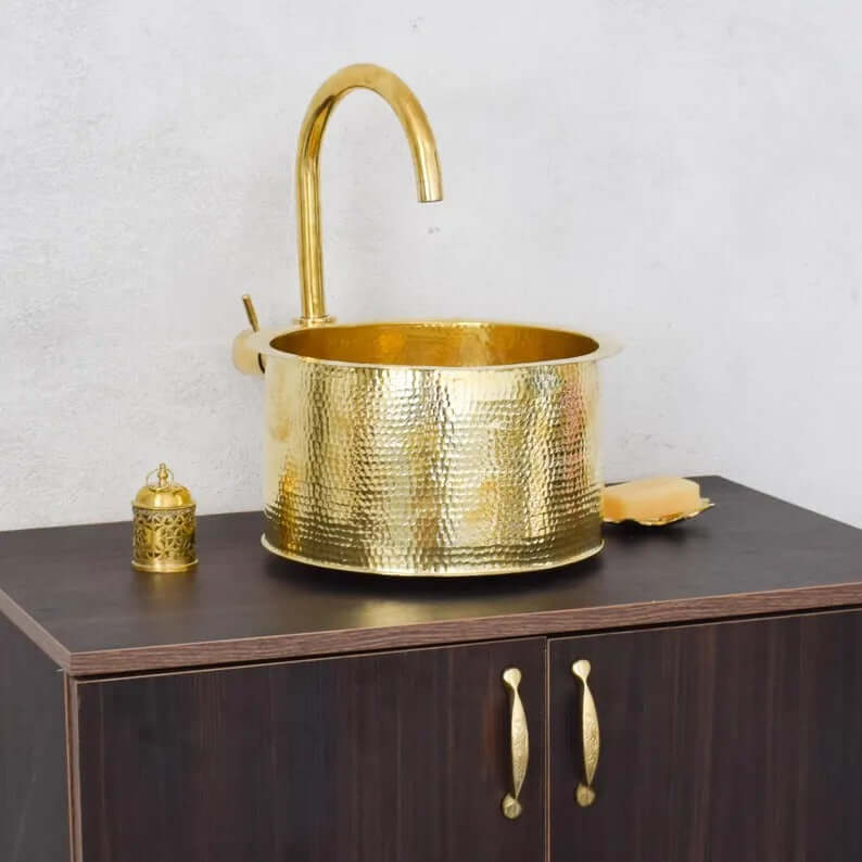 Brass handmade Moroccan sink with a sleek design on a wooden cabinet, featuring a stylish faucet and decorative items.