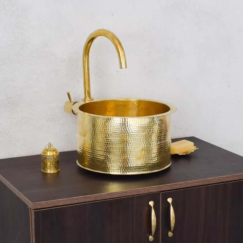 Handmade brass sink with modern faucet and decorative gold elements on wooden cabinet