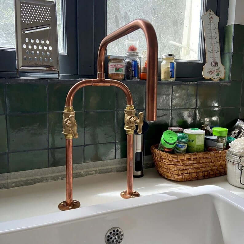 Handmade pure copper deck mount faucet with brass valves and U-shaped spout in a rustic kitchen setting.