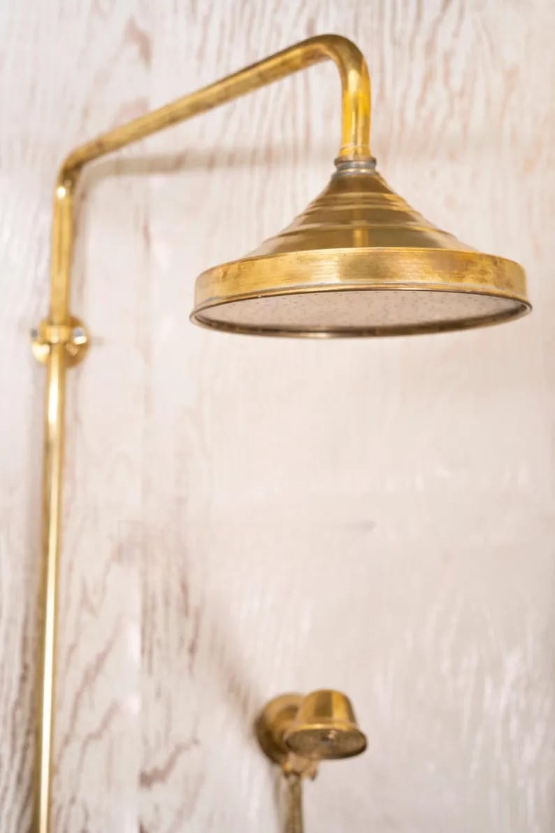 Unlacquered brass shower head with vintage design, showcasing intricate craftsmanship for a timeless bathroom aesthetic.