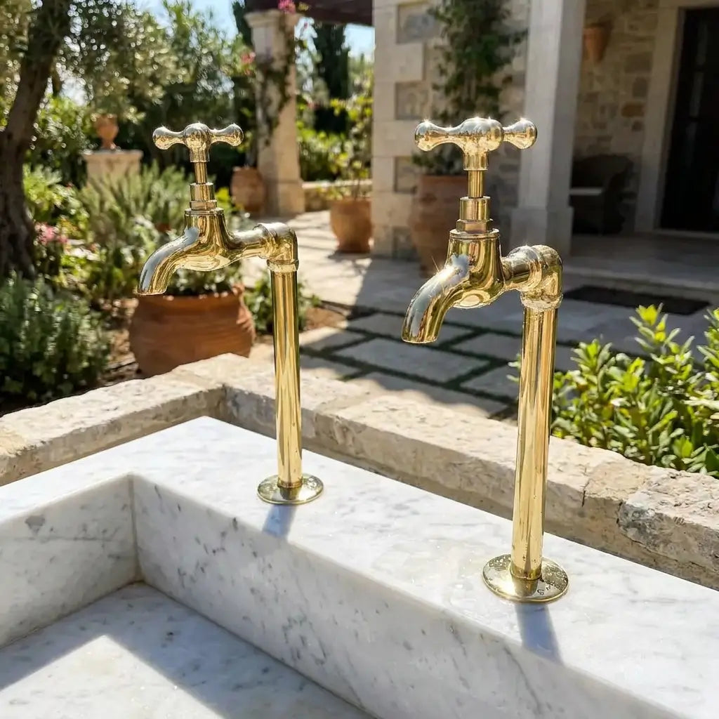 Premium polished brass water filter taps with traditional cross handles fitted on a light stone outdoor sink in a sunny mediterranean garden setup.