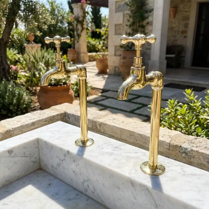 Premium polished brass water filter taps with traditional cross handles fitted on a light stone outdoor sink in a sunny mediterranean garden setup.