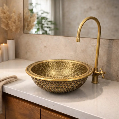Round hand hammered brass vanity bowl on a white quartz top with a warm wood cabinet and a mirror.