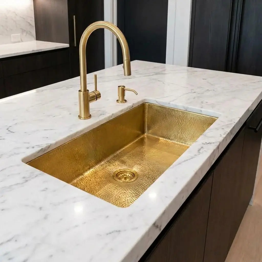 Close-up view of a golden brass undermount sink on a white marble kitchen island with an elegant arched gold faucet