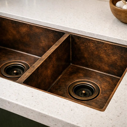 Close up view of handmade antique copper kitchen sink basin showing dual bowl design and drain details