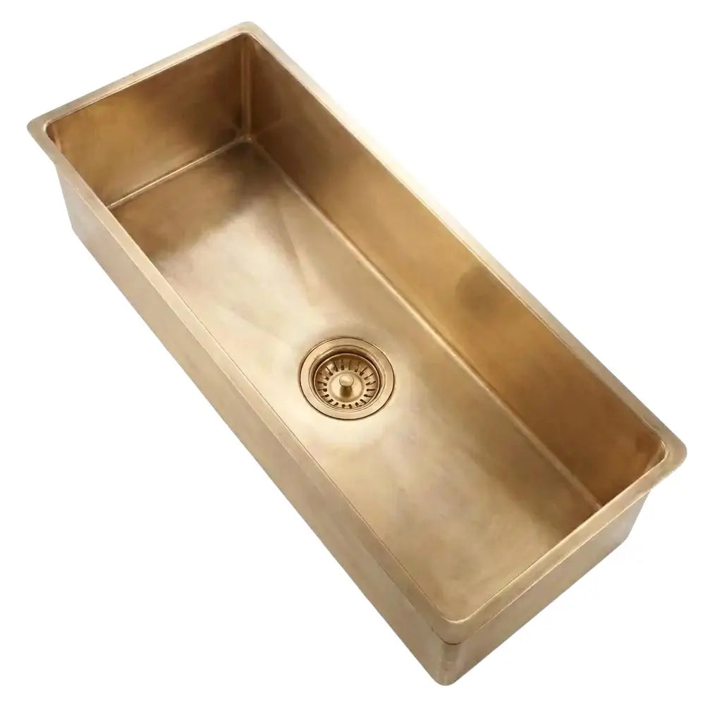 Angled top view of a deep single bowl brass kitchen sink showing its square edges and brushed metal finish on a light background