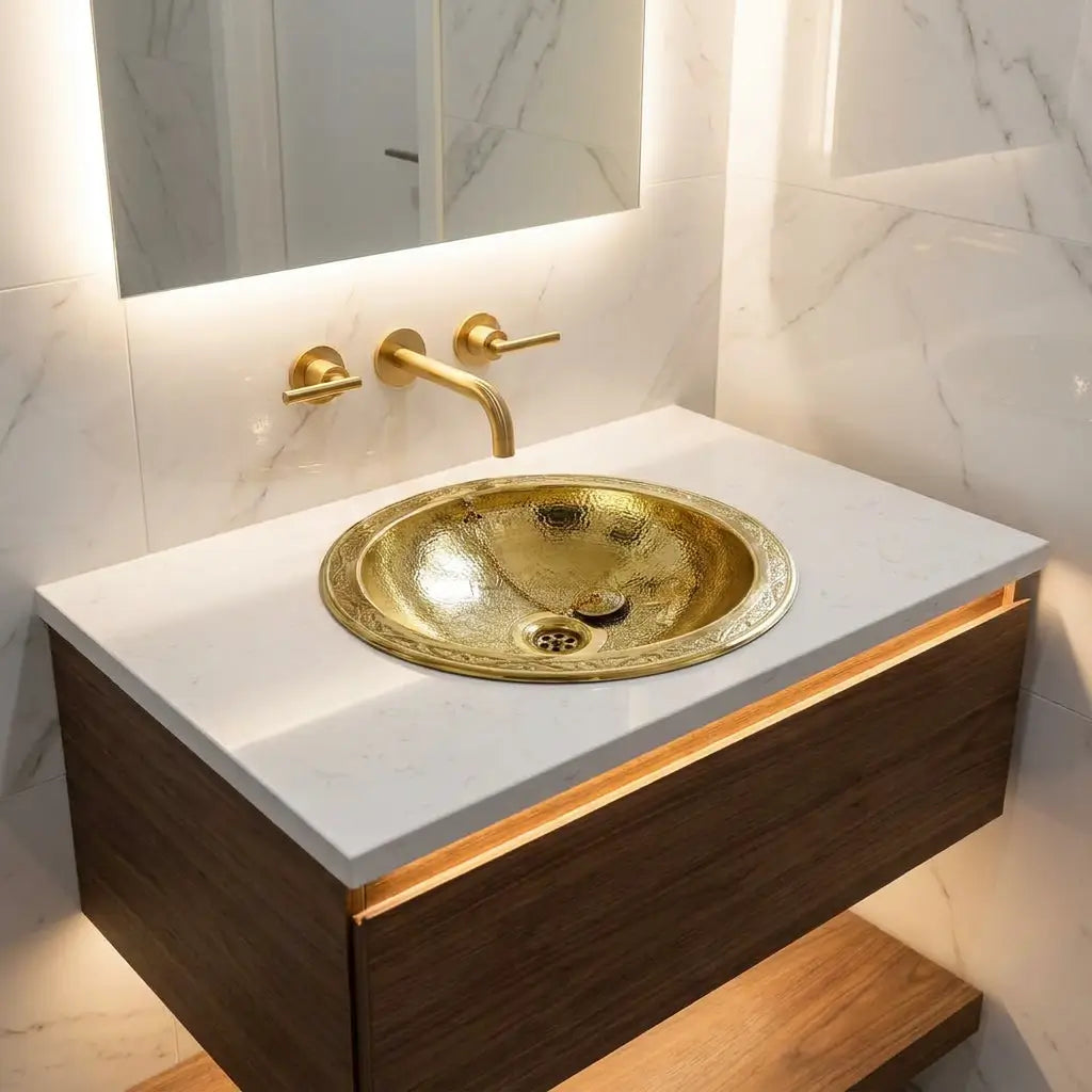 Engraved gold brass drop-in vanity sink with wall-mounted 3-hole faucet set on white quartz countertop and floating oak cabinet
