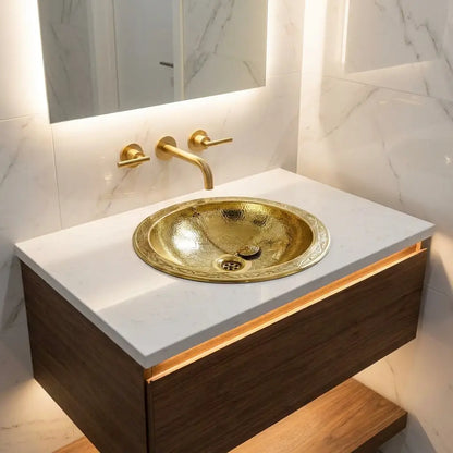 Engraved gold brass drop-in vanity sink with wall-mounted 3-hole faucet set on white quartz countertop and floating oak cabinet