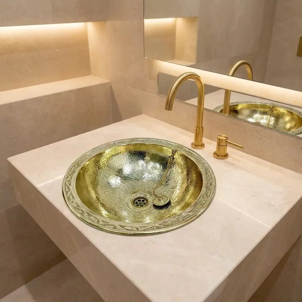 Round brass vessel sink with a hammered finish and engraved rim installed on a sleek white vanity with a modern gold gooseneck faucet.