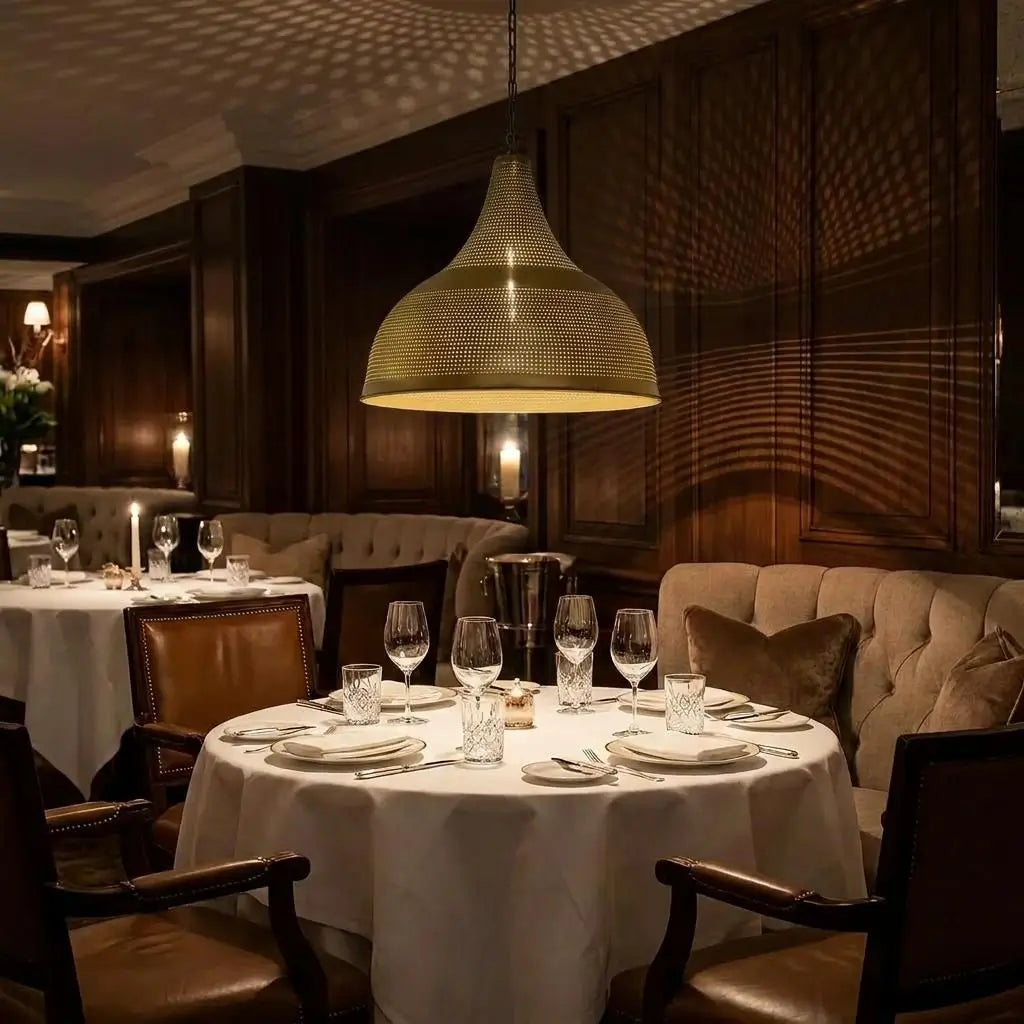 An illuminated Moroccan brass dome lamp hanging directly over a round restaurant table with a white tablecloth, wine glasses, and leather chairs in a moody fine dining room.