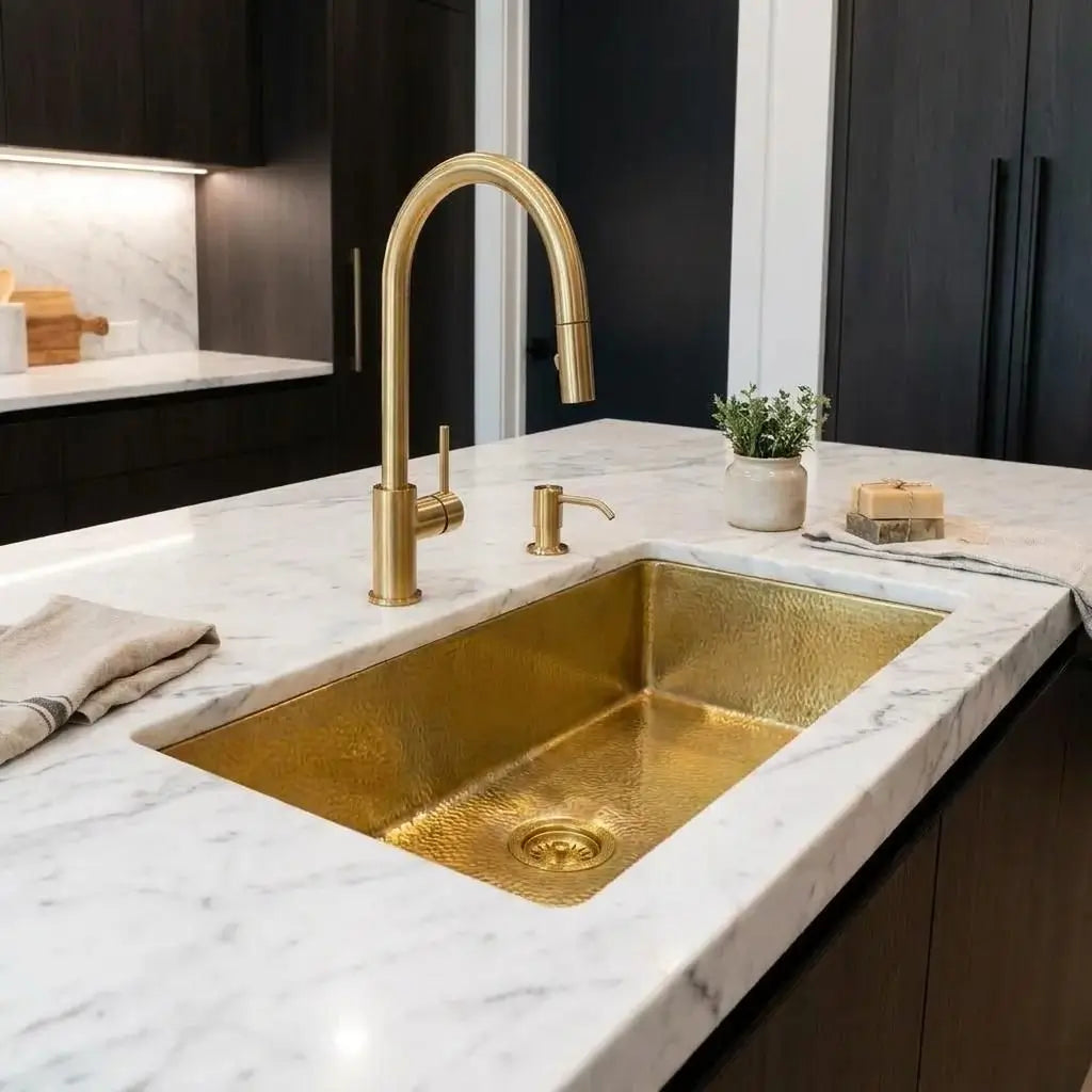 Golden brass undermount sink installed on a modern white kitchen island with a matching gold faucet against a dark wall backdrop