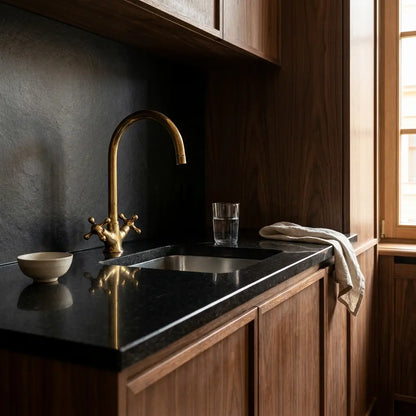 Handmade brass Moroccan vanity tap with a gooseneck spout and double cross handles installed on a glossy black countertop in a modern wooden kitchen.
