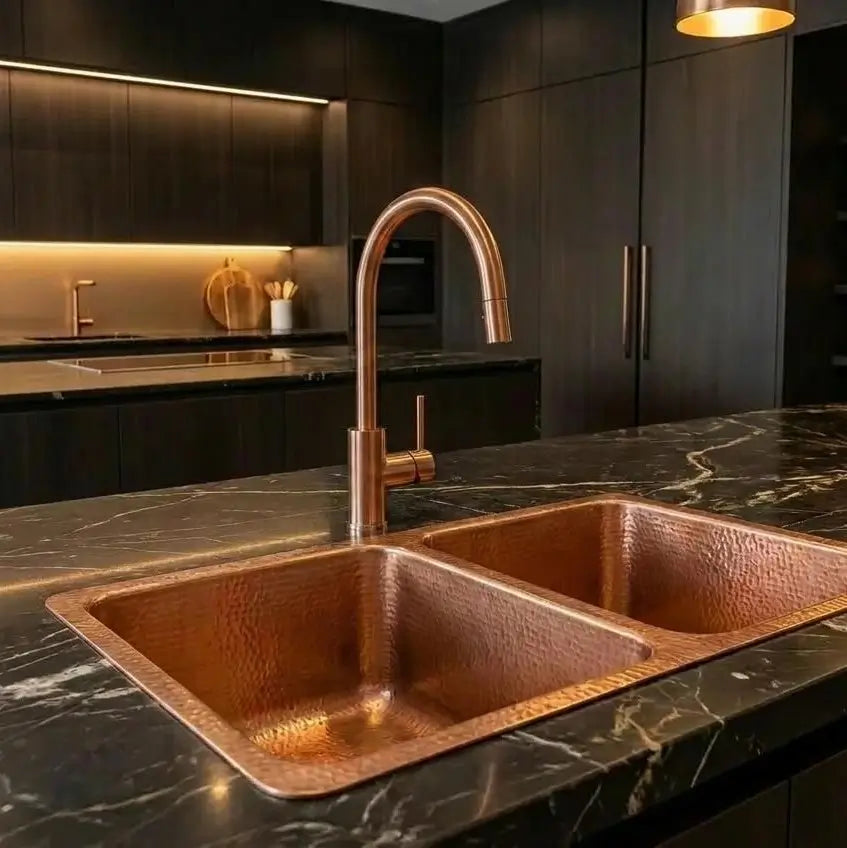 Handcrafted hammered copper double kitchen sink integrated into a dark marble countertop with a copper gooseneck faucet in a luxury kitchen.