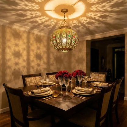 Handcrafted Moroccan brass ceiling light fixture with colorful glass hanging over a set dining table, reflecting intricate oriental patterns on surrounding walls.
