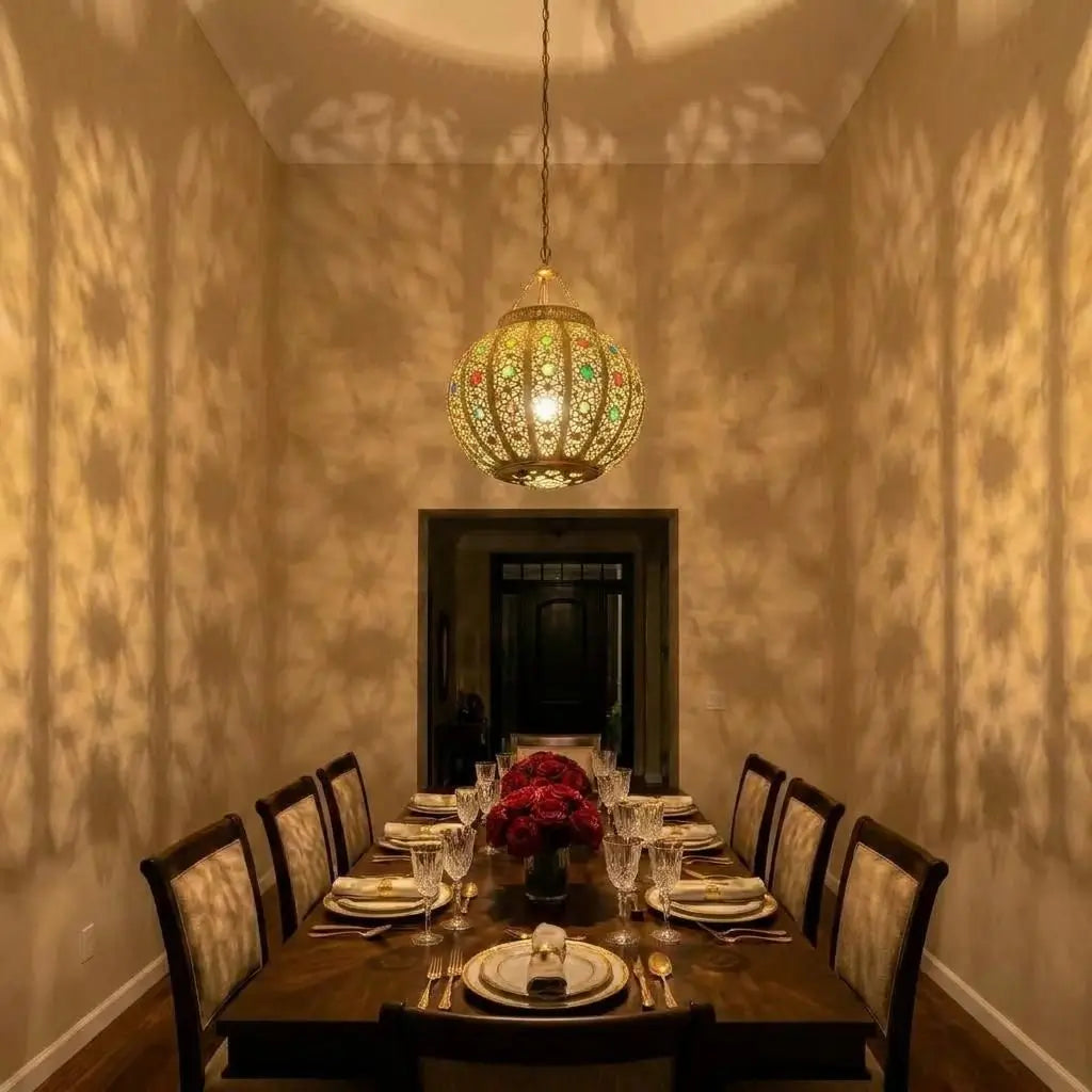 Handmade brass lampshade with colorful glass accents hanging in a long narrow dining room, casting precise geometric patterns of light and shadows on the side walls.