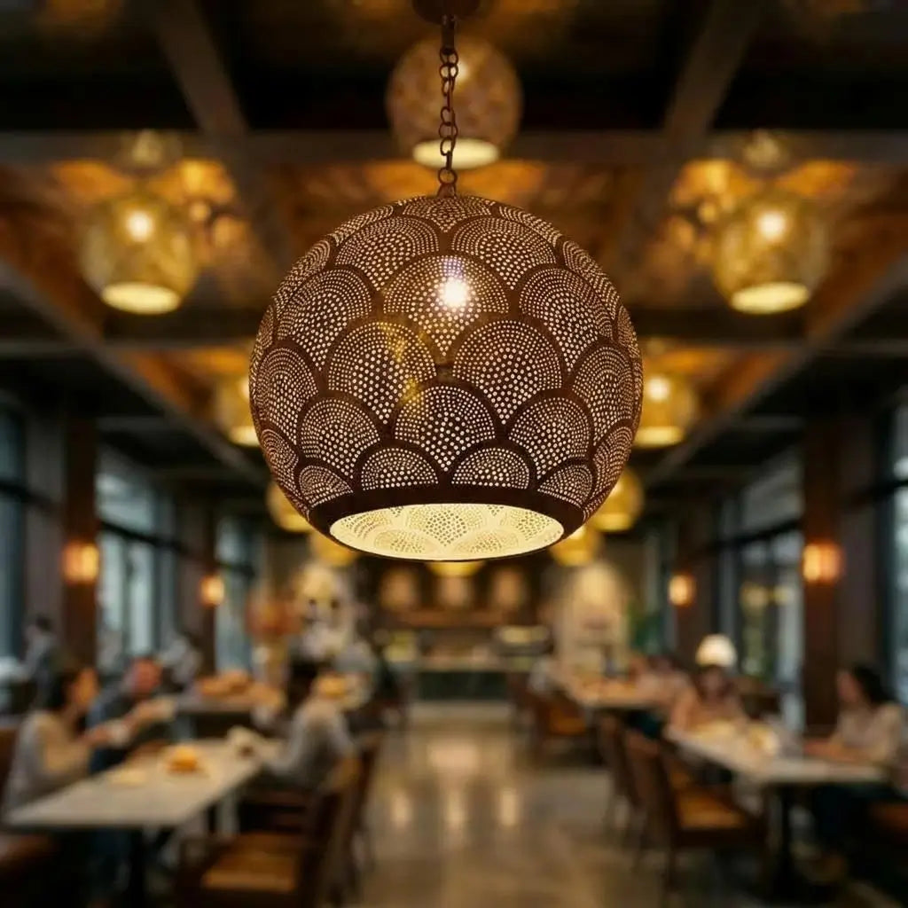 Close-up of an artisan handmade brass pendant light with fish scale perforations hanging in a blurred restaurant background