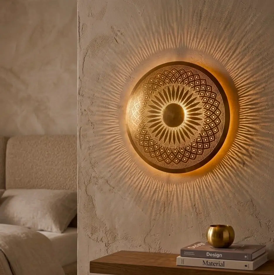 Handmade Moroccan brass wall sconce casting vibrant radial shadows on a bedroom wall above a nightstand with books.