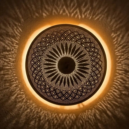 Handmade Moroccan brass wall sconce illuminated from behind, casting complex geometric and radial light shadow patterns.