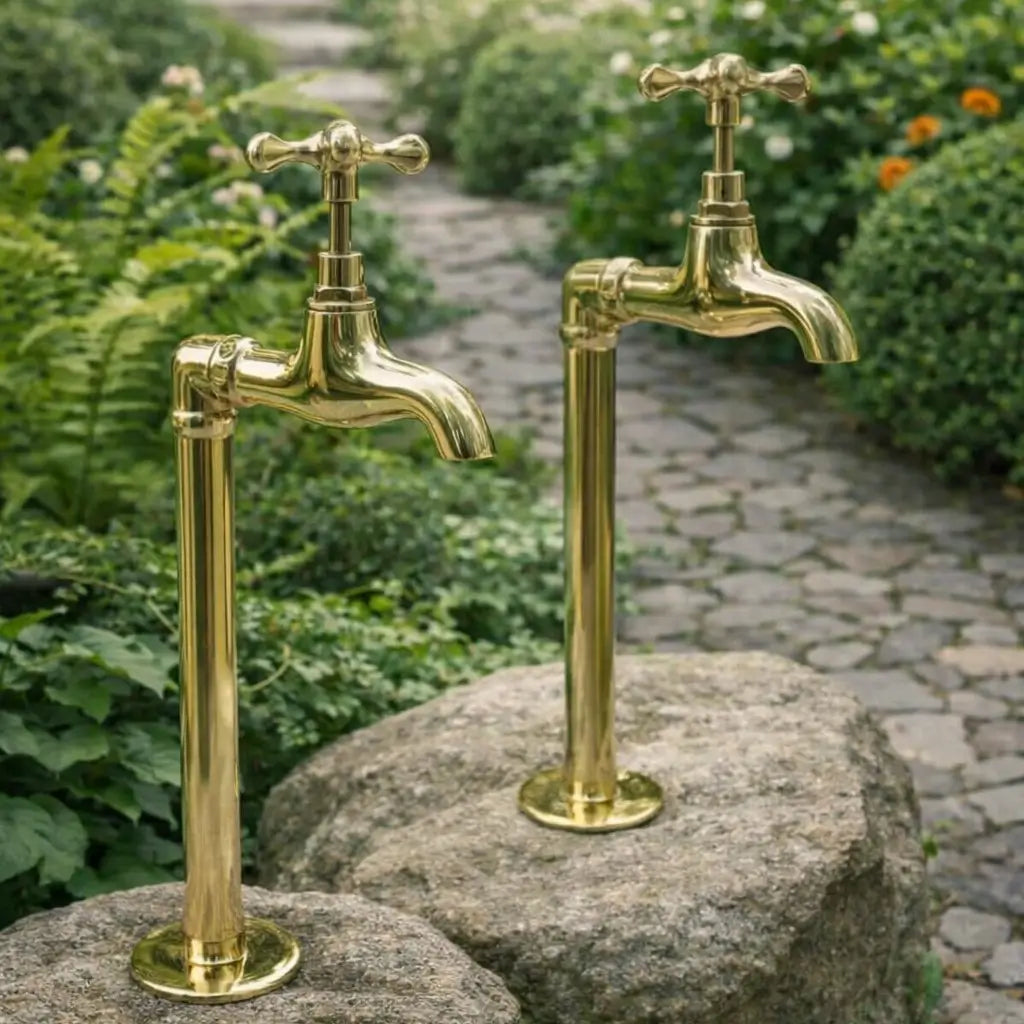Two handmade unlacquered brass water dispenser faucets mounted on large boulders along a stone garden pathway