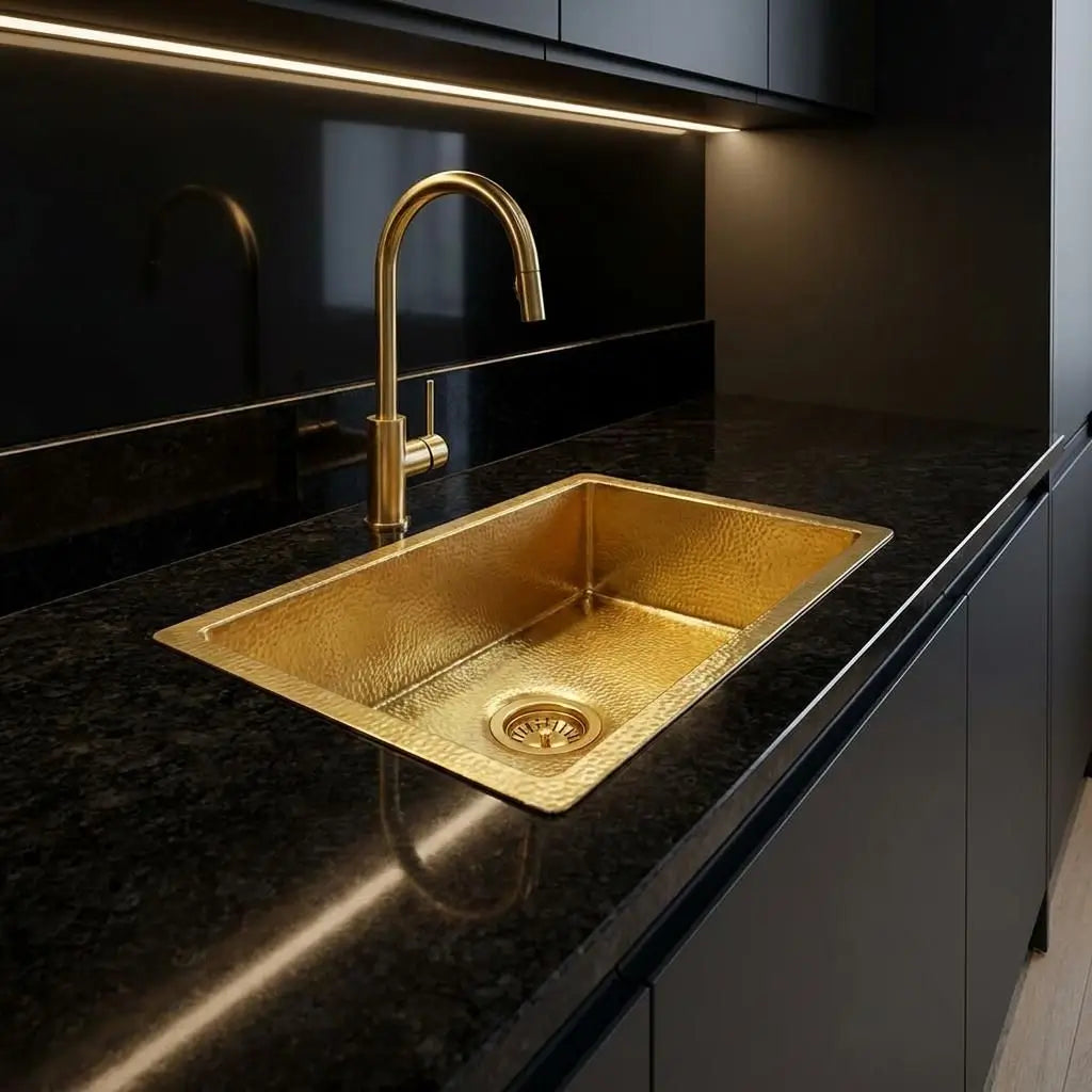Luxury golden brass undermount sink embedded in a polished black marble countertop inside a modern dark kitchen setup