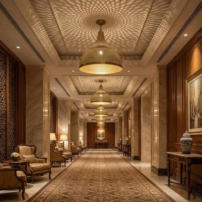 A series of luxury Moroccan brass dome chandeliers installed along a grand hotel hallway ceiling, casting ornate geometric shadow patterns over marble walls and carpeted floors.