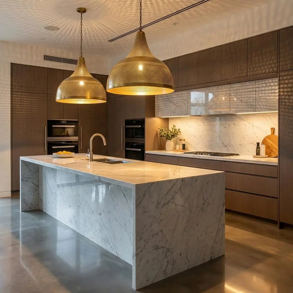 A pair of large Moroccan brass dome pendant lights hanging above a modern luxury kitchen marble island, casting a warm golden glow over unlacquered wood cabinetry and a white countertop.