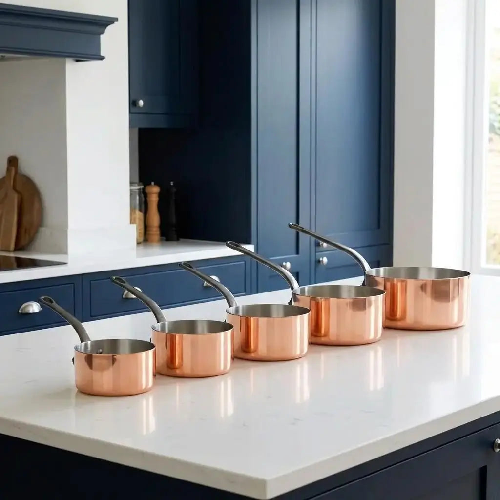 Five-piece Moroccan copper cookware set with shiny tin lining displayed on a white marble countertop in a modern luxury kitchen with navy blue cabinets.