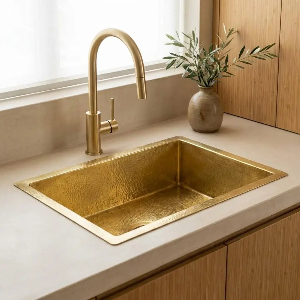 Minimalist golden brass undermount sink installed on a clean white quartz countertop with a contemporary gold faucet and a small ceramic vase