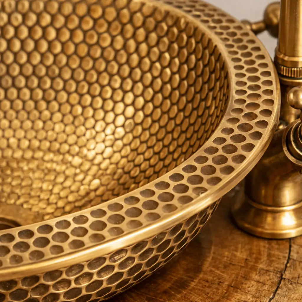 Close-up macro shot of a modern custom made brushed brass bathroom sink, highlighting the intricate handcrafted honeycomb hammered texture and high-quality metal finish.
