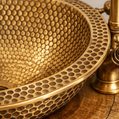 Close-up macro shot of a modern custom made brushed brass bathroom sink, highlighting the intricate handcrafted honeycomb hammered texture and high-quality metal finish.