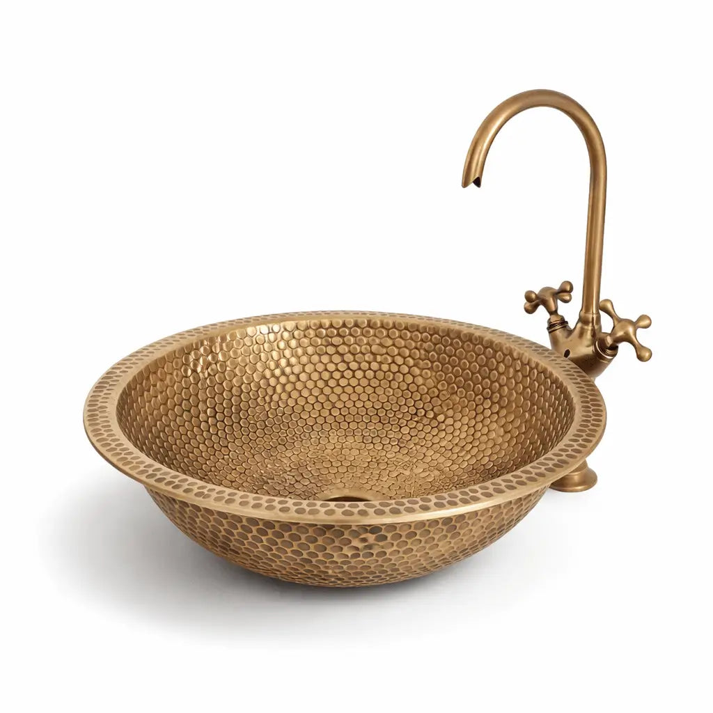 Modern custom made brushed brass bathroom sink with a detailed honeycomb hammered finish, paired with a tall antique brass faucet on the right side, completely isolated on a pure white studio background for a clean e-commerce look.