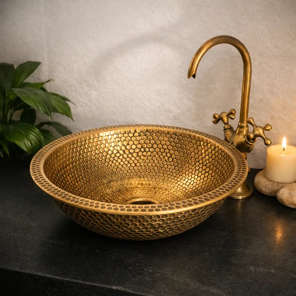 Modern custom made brushed brass bathroom sink featuring a detailed honeycomb hammered finish, styled with an antique brass faucet and a burning candle on a premium black countertop.
