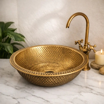 Premium custom made brushed brass bathroom sink with detailed honeycomb textures, set on a modern white marble vanity countertop under soft ambient light.
