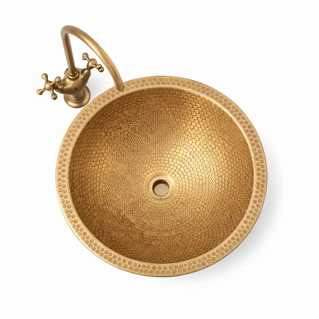 Top-down studio product view of a modern custom made brushed brass bathroom sink and antique brass faucet, highlighting the perfect circular honeycomb hammered pattern on a pure white background.