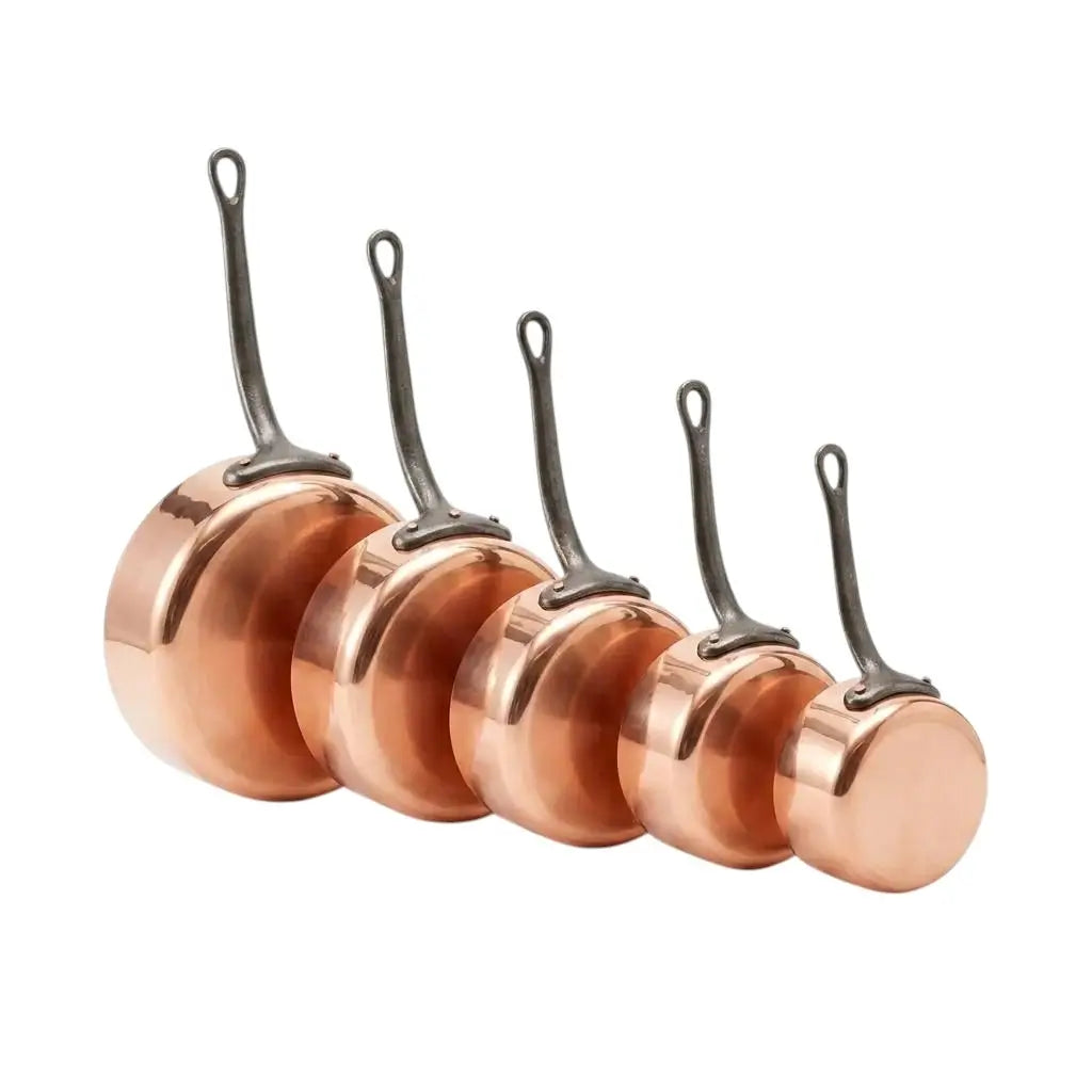 Five graduated sizes of Moroccan copper saucepans stacked together on a clean white background, showcasing heavy gauge construction, artisan craftsmanship, and long sturdy handles.