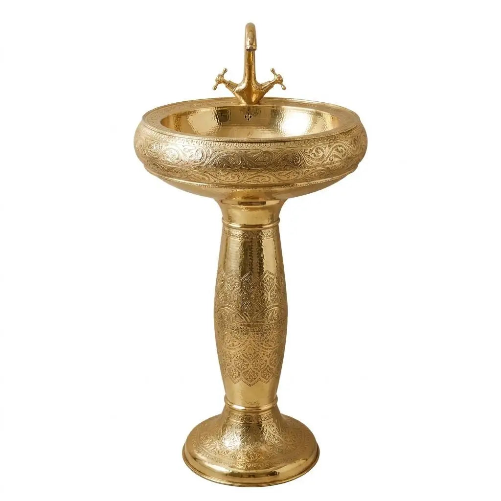 Hand-engraved Moroccan brass pedestal sink with a matching antique brass double-handle faucet, featuring intricate traditional artisanal geometric patterns, isolated on a clean neutral white background.