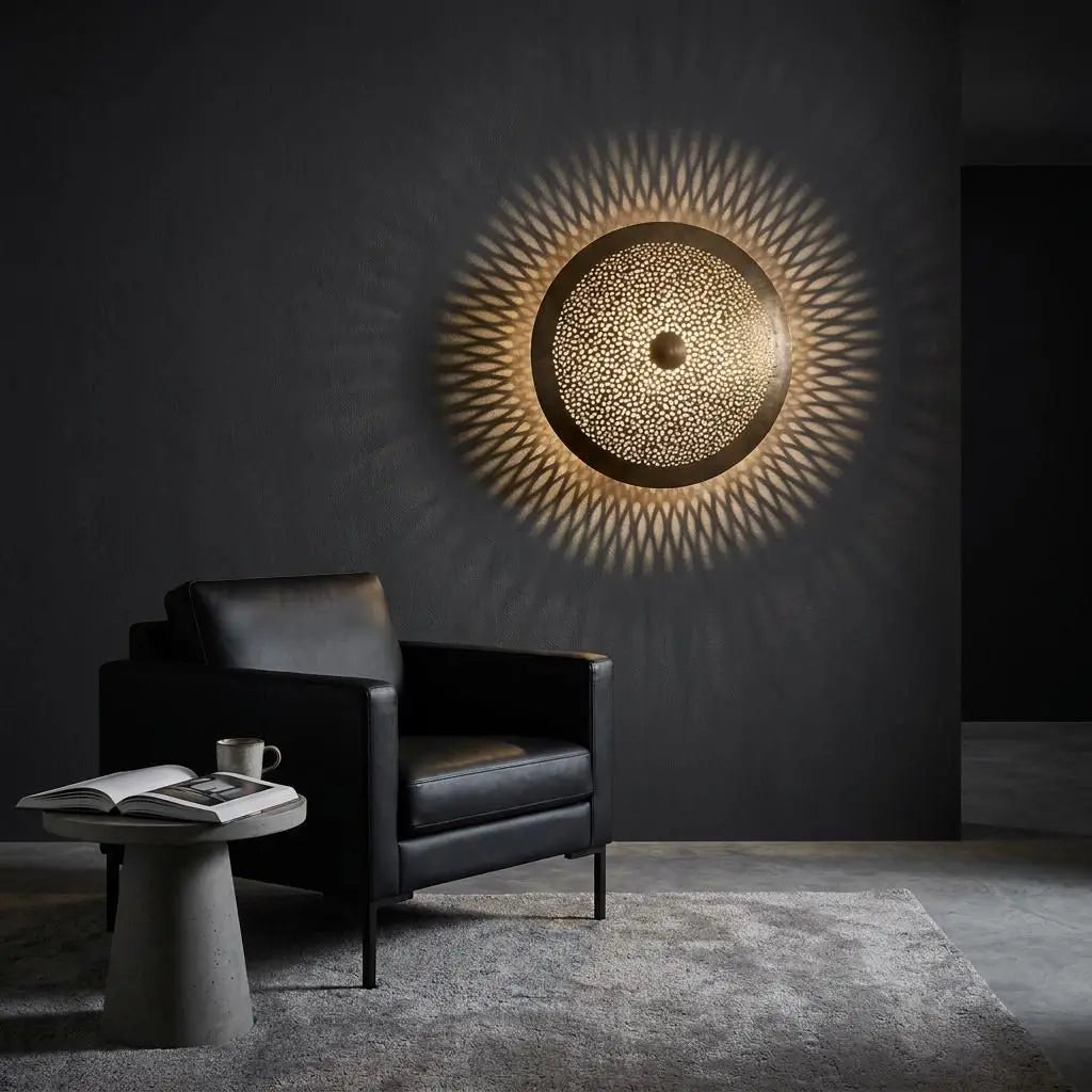 Moroccan wall light displaying handmade artisan brass lighting with a glowing sunburst shadow effect on a dark gray living room wall next to an armchair.