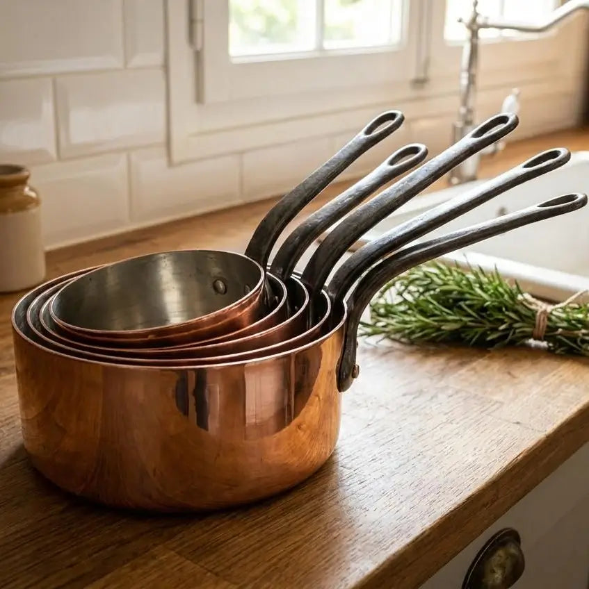 Five-piece Moroccan copper saucepan set nested inside each other on a wooden kitchen counter, demonstrating space-saving storage, thick tin lining, and sturdy cast iron handles.
